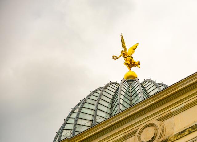 Ein goldener Engel, der auf einer Kuppel steht. Er hebt ein Bein in die Luft und in der Hand hält er einen Lorbeerkranz. Dresden, Brühlsche Terasse, Kunstakademie, Zitronenpresse