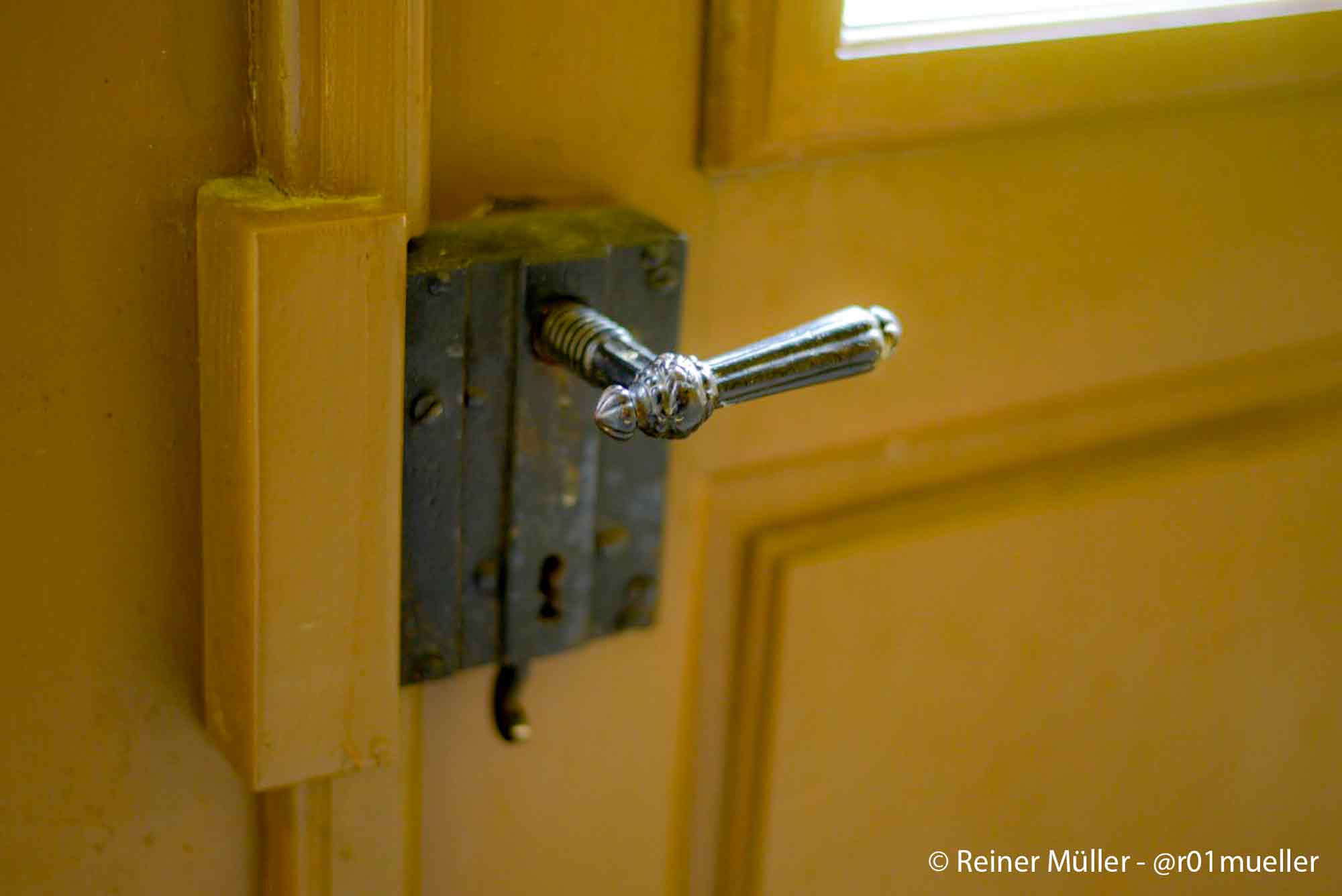 Eine alte Türklinke an einer Holztür mit Fenster