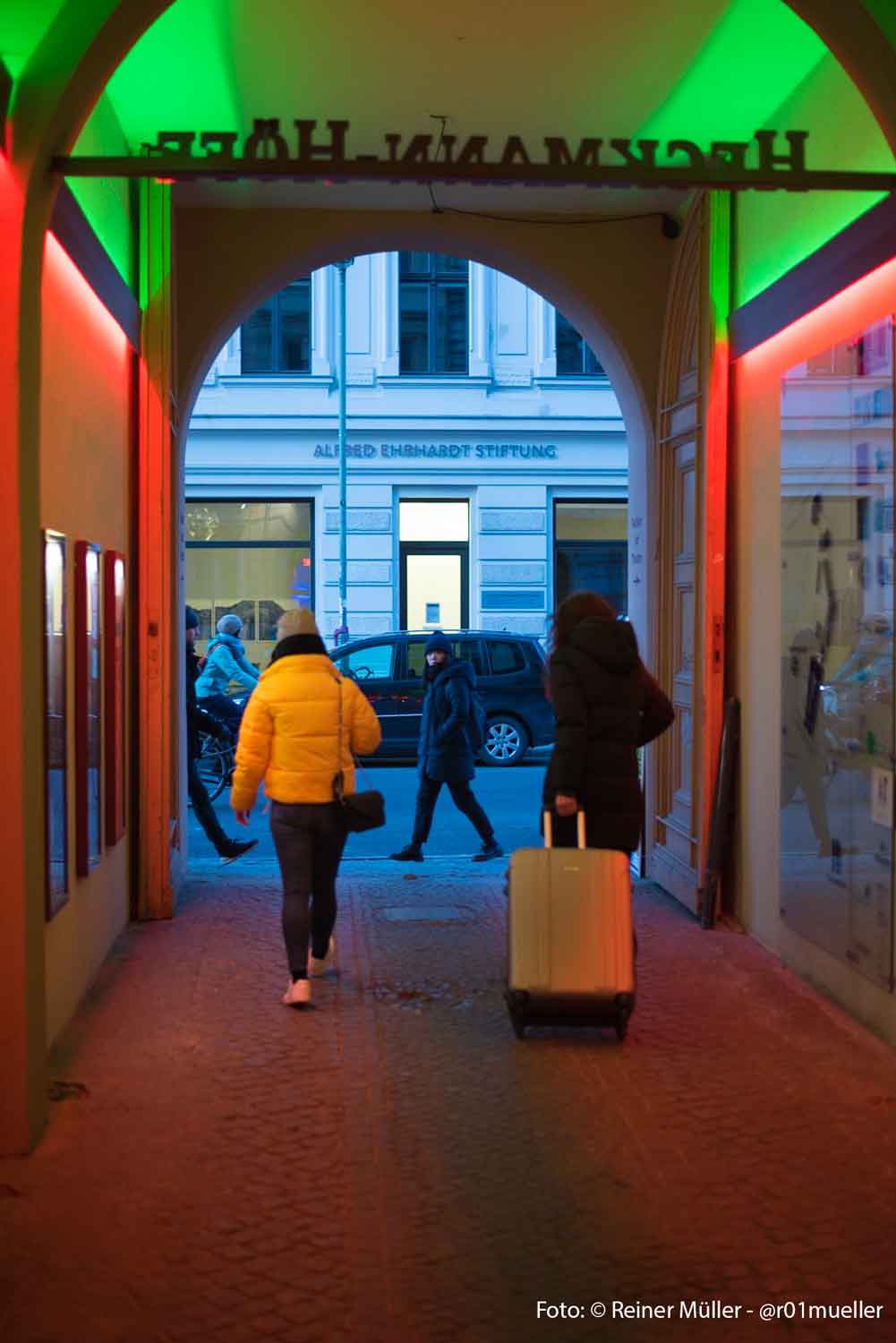 Zwei Frauen laufen aus einem Hauseingang auf die Straße, auf der andere Menschen unterwegs sind.